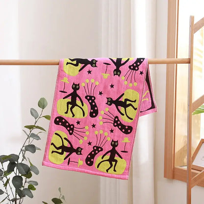 Pink cotton gauze hand and face towel with black and yellow cartoon cats on wooden rack from decorbites bathroom set