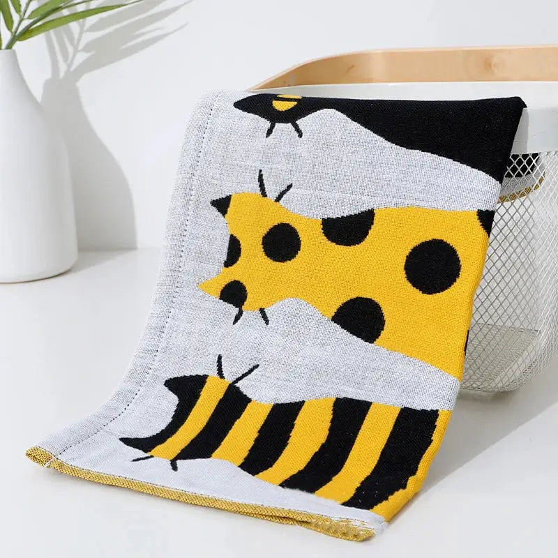 Soft knitted baby blanket with yellow and black bees pattern on gray background paired with decorbites cotton gauze face towel
