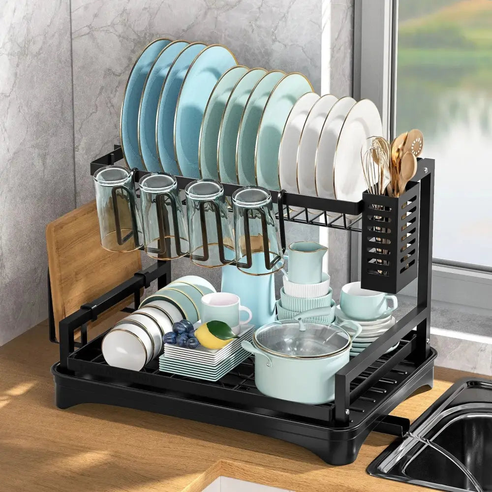 Two-tier black metal dish drying rack with drainboard organized with hanging glassware and stacked plates