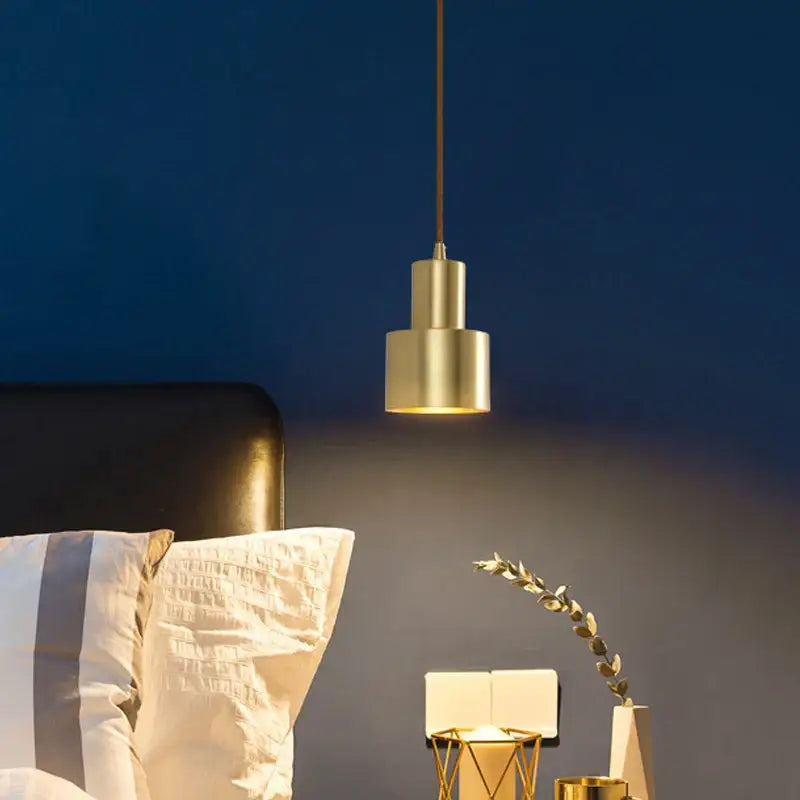 A two tier brass finish pendant light with a modern cylindrical design hangs against a dark blue wall decorbites brass finish