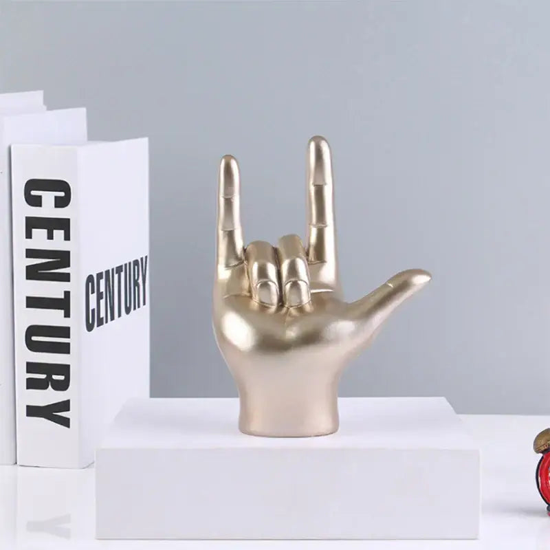 Gold-colored resin decorbites abstract hand love sculpture in rock gesture displayed on a white pedestal for living room decor