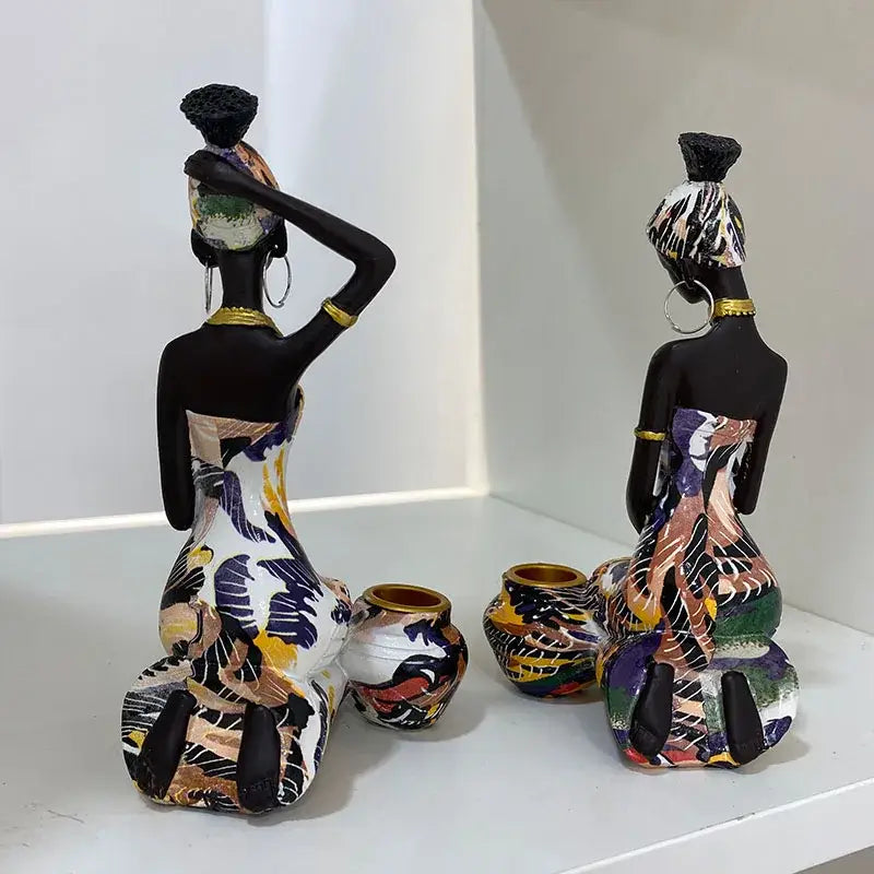 Two stylized decorbites black woman candlestick figurines with black painted skin and colorful dresses on white shelf