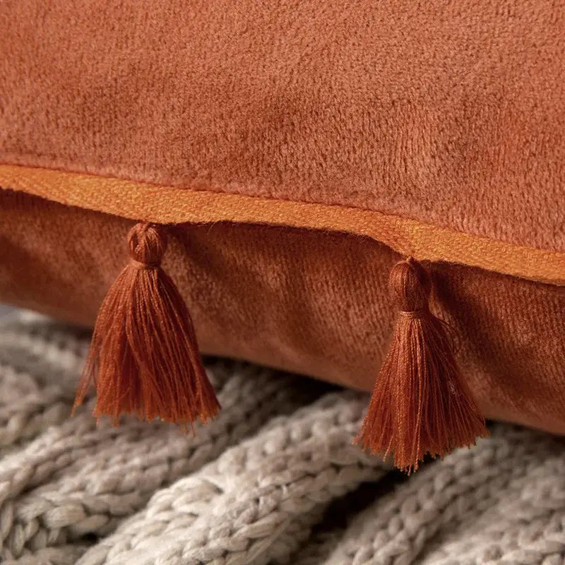 A rust-colored tassel velvet pillow with fringed tassel edges for living room decor by decorbites