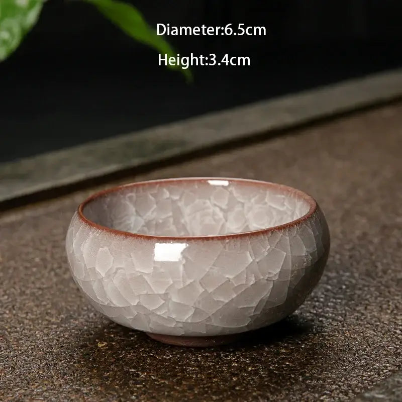 A small handcrafted ceramic tea bowl with soft gray and brown tones featuring decorbites ice cracking glaze design