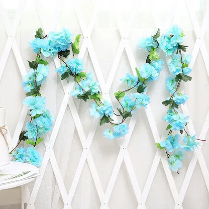 Light blue artificial hydrangea rose flowers vine garland with green leaves and dark stems on white lattice backdrop