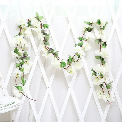 A delicate white artificial rose flowers vine garland with green leaves and brown stems for living room decor