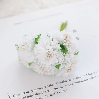 A delicate white floral hair clip with tiny green leaves and cream accents featuring decorbites carnation stamen silk flowers