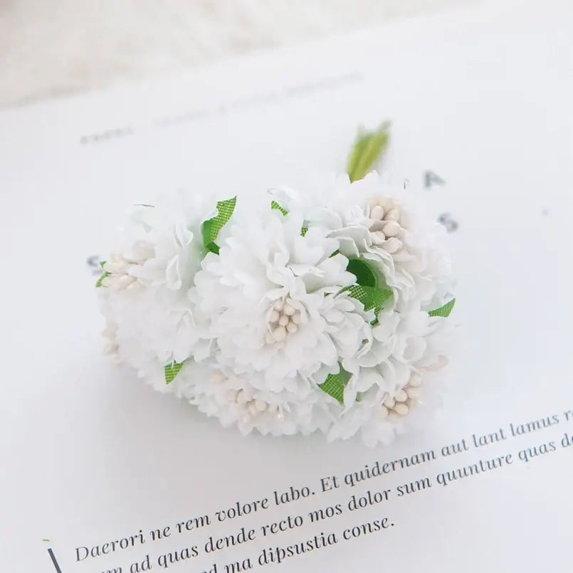 A delicate white floral hair clip with tiny green leaves and cream accents featuring decorbites carnation stamen silk flowers