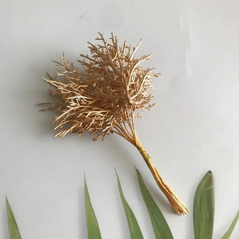 Golden metallic branch decoration with intricate twig-like branches complements vibrant dried flower bouquets in white vase