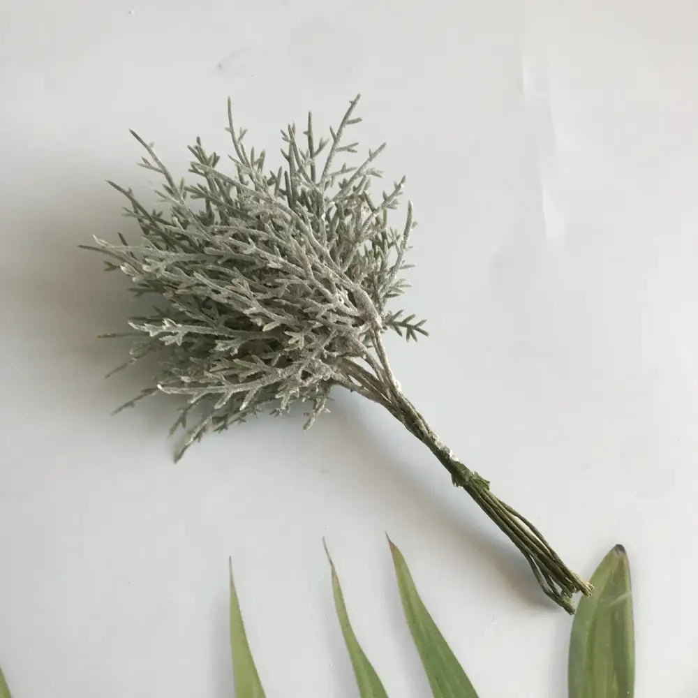 A delicate silvery-gray artificial plant with feathery branches in a vibrant multicolored dried flower bouquet in white vase