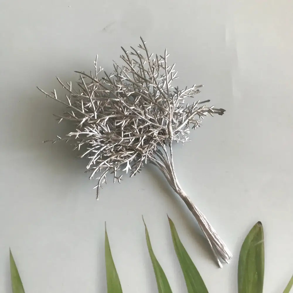 Silver metallic branch brooch with intricate twig detailing displayed alongside vibrant dried flower bouquets in white vase