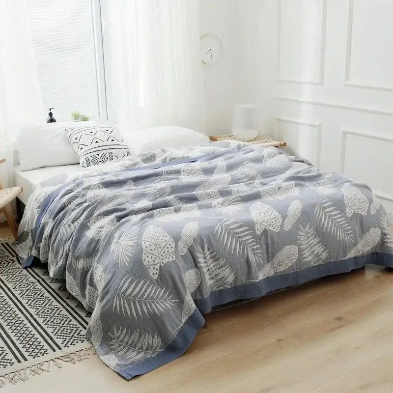 Gray throw blanket with white leaf patterns and blue border paired with vibrant orange and gold geometric nordic throw blanket