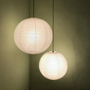 Two off-white spherical akari rice paper pendant lights hanging from black cords against a muted green wall
