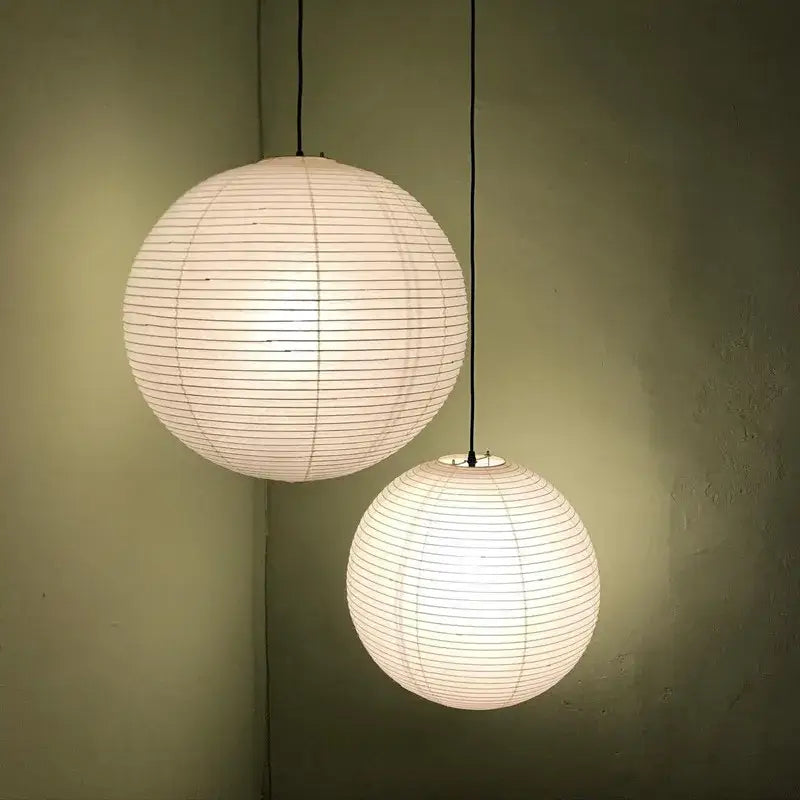 Two off-white spherical akari rice paper pendant lights hanging from black cords against a muted green wall