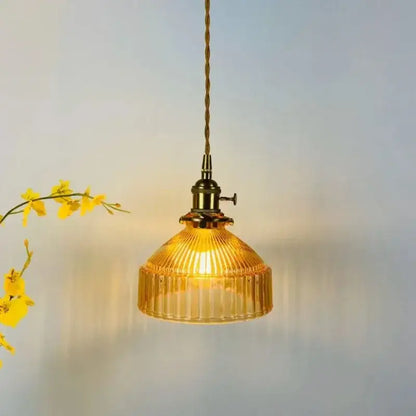 A warm amber colored glass pendant light with vertical ridges and brass-finished metal fixture for dining room