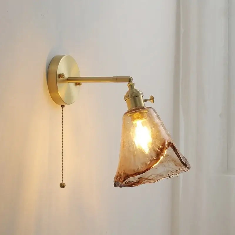A warm-toned vintage amber glass copper led wall lamp with brass arm and pull chain for bedroom use