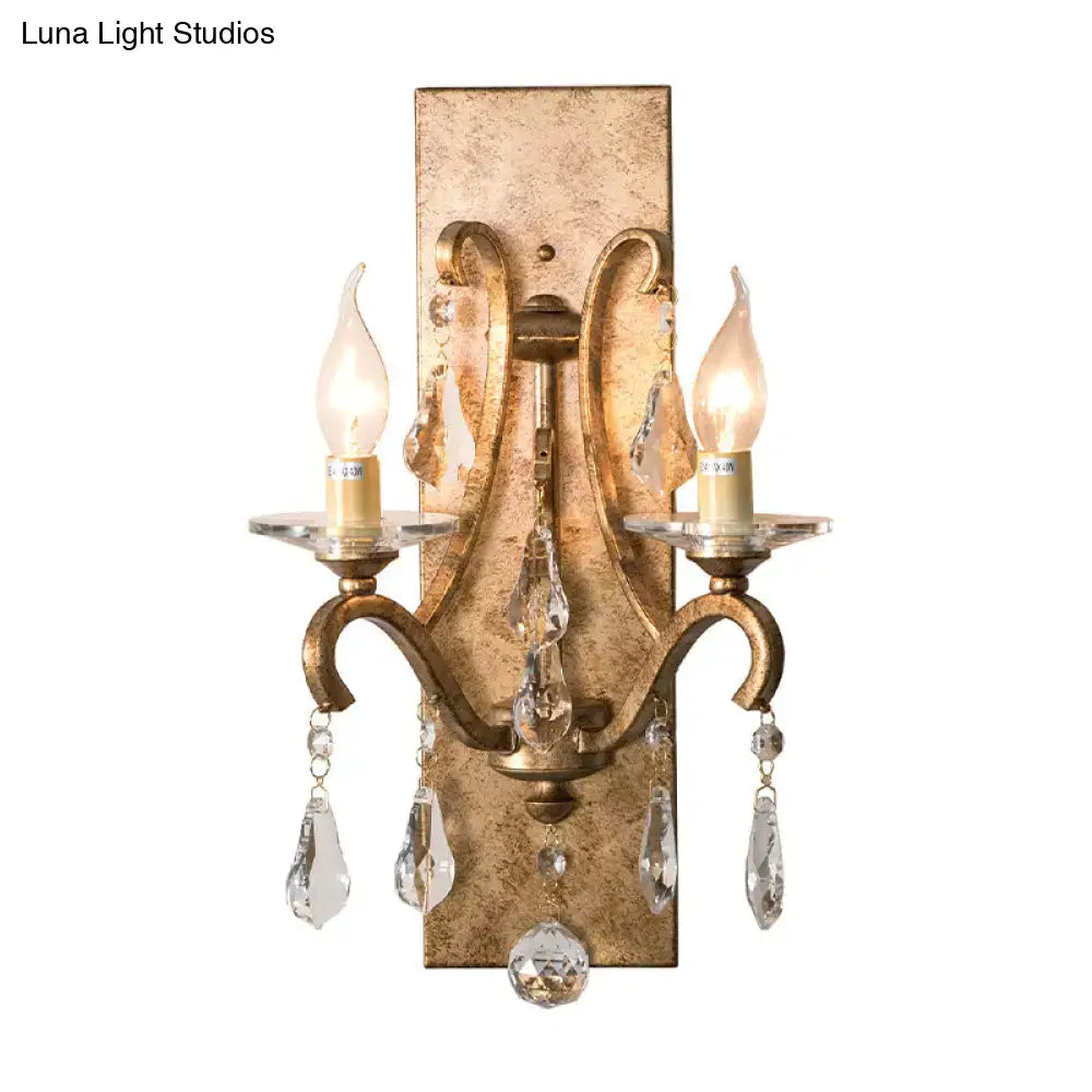Antique brass two-light wall lamp with crystal droplets and candle-style bulbs in vintage gold and dark purple clear design
