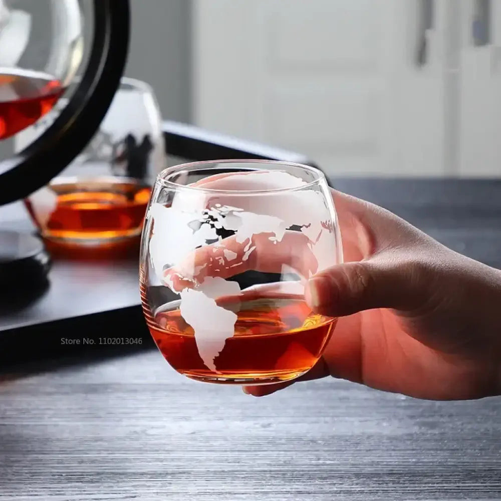 A clear glass tumbler with a frosted world map design filled with amber liquid from vintage earth decanter set