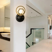 Gold-toned hexagonal wall lamp with black circular base and brass accents for living space with black finish