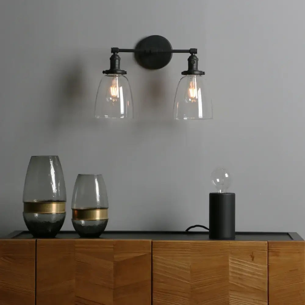 Vintage black wrought iron wall sconce with two clear glass shades and exposed filament bulbs for bedroom lighting