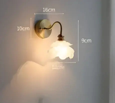 Vintage brass and amber glass led wall lamp featuring a delicate curved arm and white ceramic flower shade for bedroom use