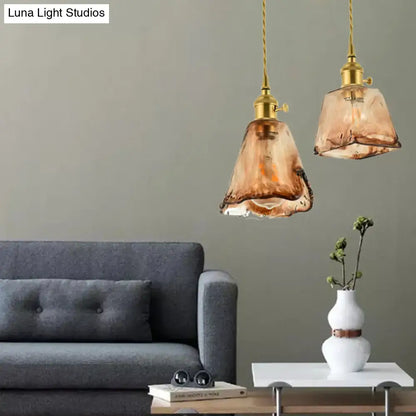 Two amber-tinted handmade glass pendant lights with brass shaded drop fixtures hang from twisted gold cords