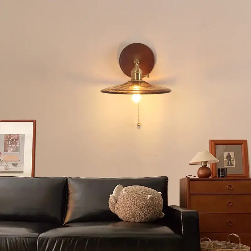 Vintage brass and amber glass wall sconce with brass finish, conical shade, circular backplate, and pull chain switch