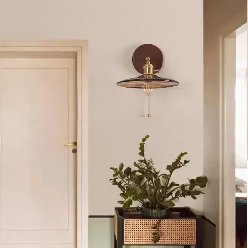 Vintage brass and amber glass wall sconce with dark brown backplate and pull chain switch for stair lighting