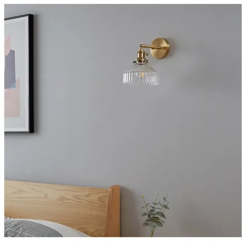 Vintage brass wall lamp with gold-toned finish, clear ribbed glass shade, and pull chain switch for bedroom use