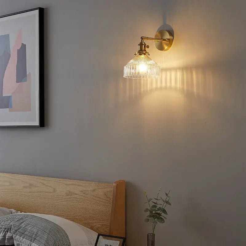 Vintage brass wall lamp with clear ribbed glass shade and pull chain switch casting warm light for bedroom use