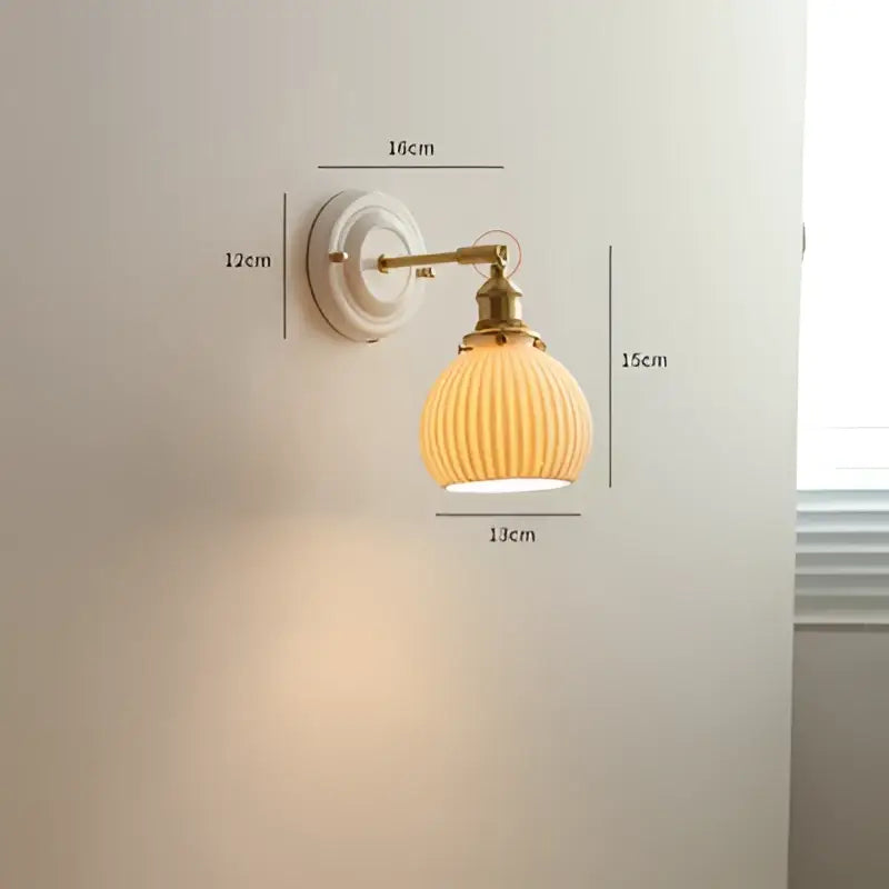 Cream-colored ribbed glass led wall light with brass-finished metal arm and mounting plate for bedroom sconce use
