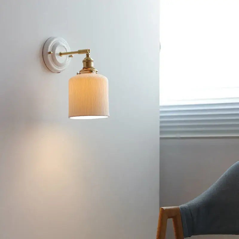 Cream-colored ribbed glass led wall light with brass accents and white ceramic wall mount for bedroom sconce