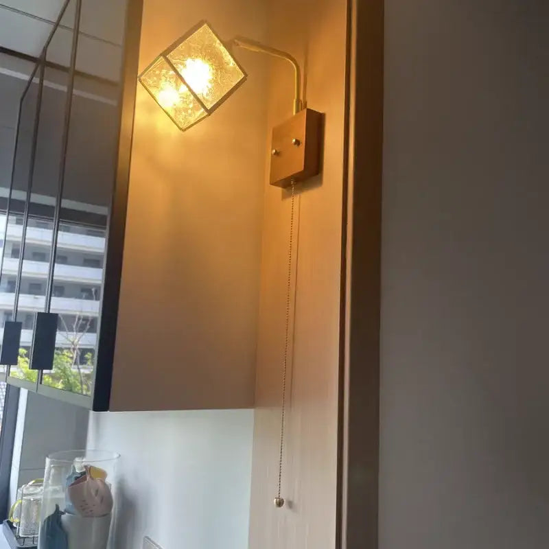 Vintage brass and walnut wall light with gold-toned pull chain switch and a square textured glass shade for bedroom use