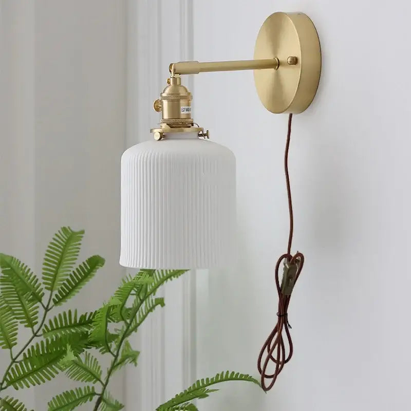 A white ribbed glass wall light with brass-finished metal arm and ceramic knob wall mount for bedroom use