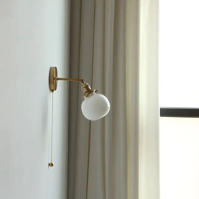 Gold-finished vintage brass wall lamp with clear glass globe and pull chain switch mounted on adjustable arm