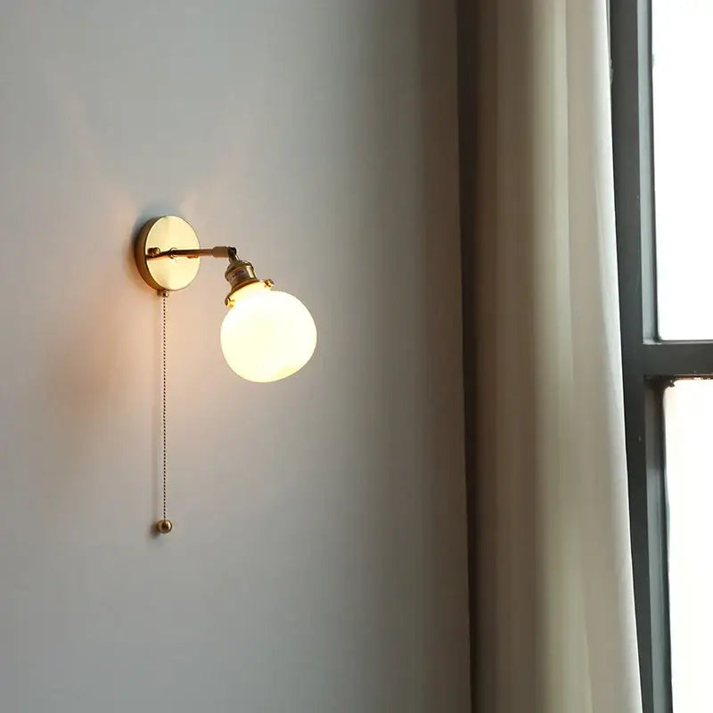 Gold-toned vintage brass wall lamp with clear glass frosted bulb and adjustable arm featuring pull chain switch for bathroom