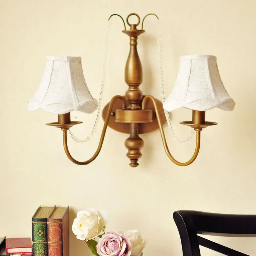 Antique brass two-light wall sconce with white fabric shades and crystal bead chains for vintage bedroom candle light