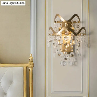 Vintage brass crystal wall sconce with direct wired power source, gold-toned wavy frame, bulb base, and dangling crystals