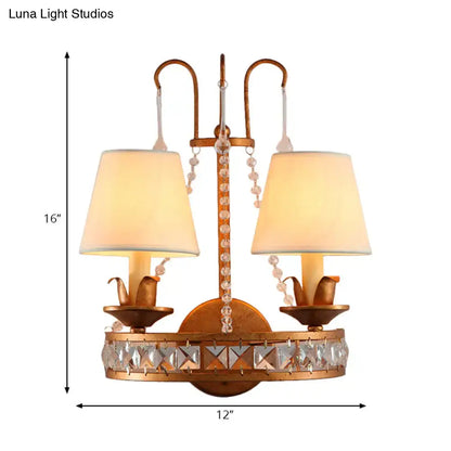 Antique brass finish two-light wall lamp with crystal accents and cream fabric shades for vintage bedroom sconces