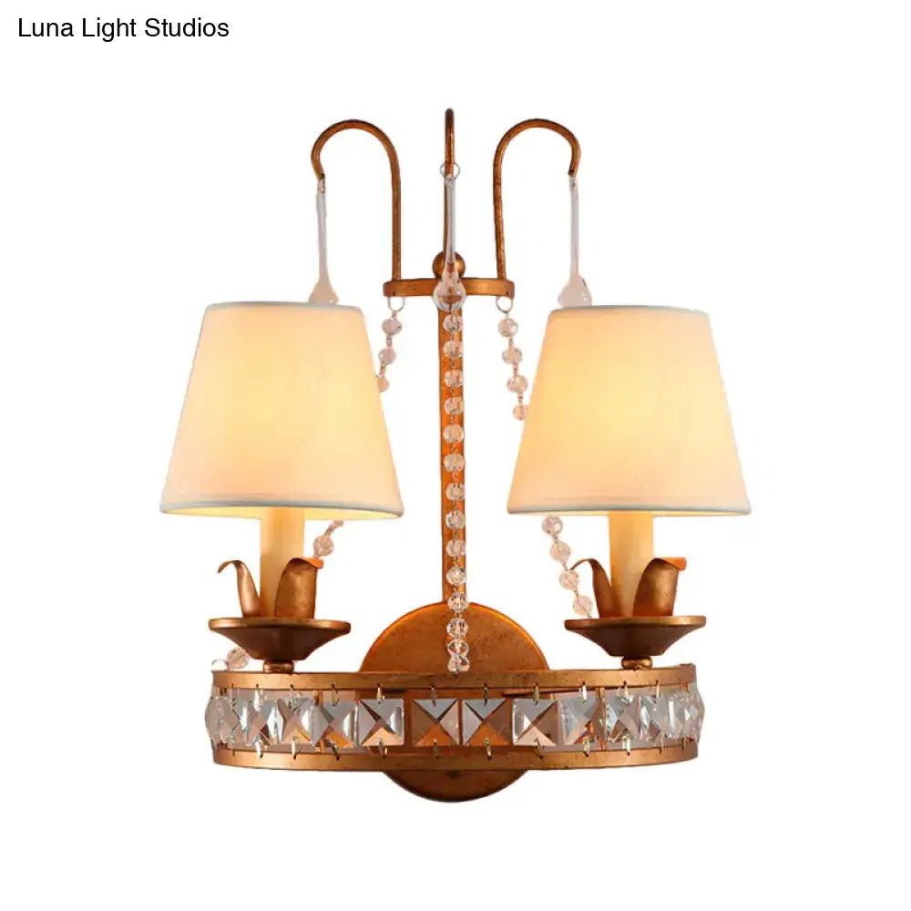Antique brass finish wall lamp with two lights, crystal accents, and cream fabric shades for vintage bedroom decor