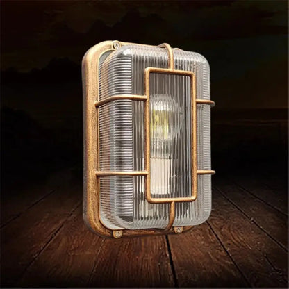 Industrial-style vintage brass gas station canopy wall light with clear ribbed glass and metal cage frame for outdoor use