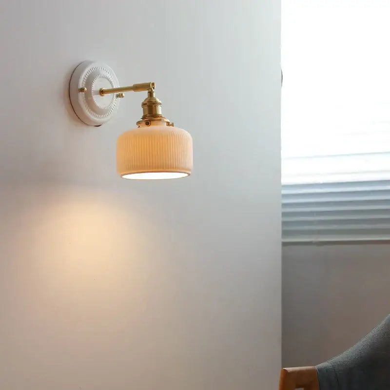 Vintage brass globe wall sconce with cream-colored ribbed glass and brass hardware mounted on a white wall plate