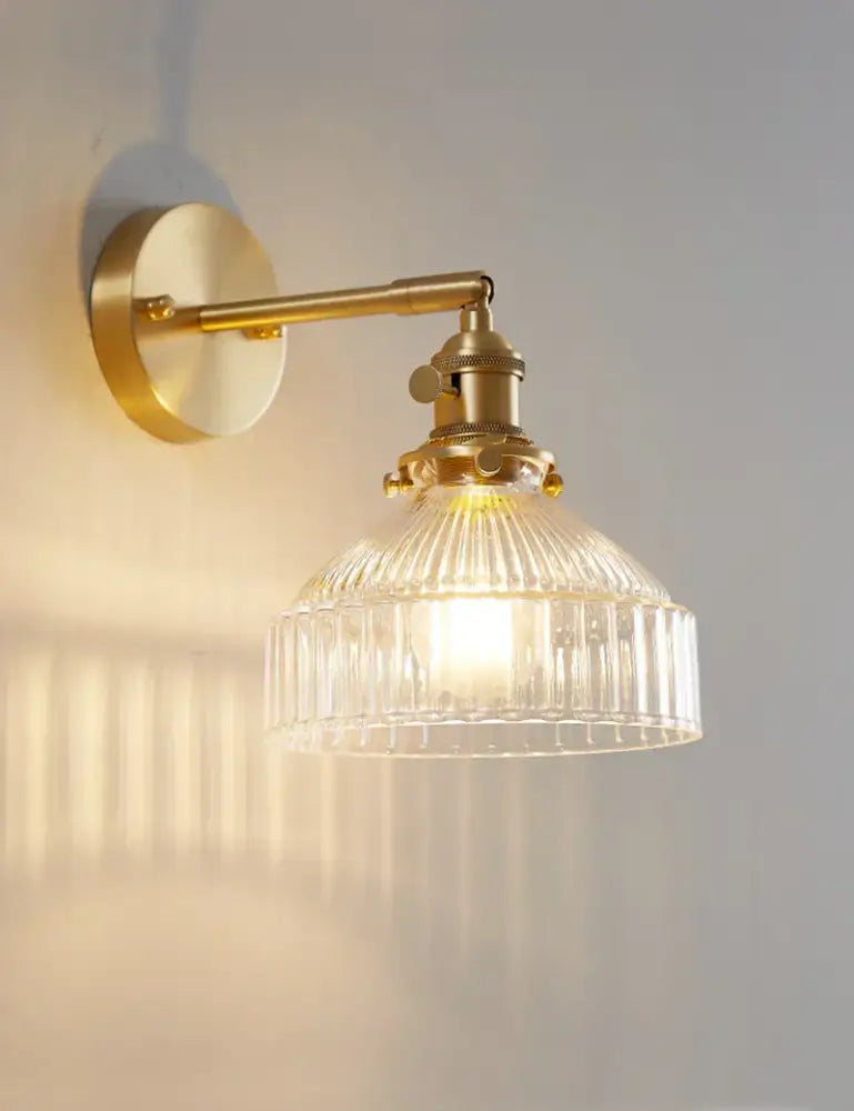Vintage brass wall sconce with clear ribbed glass shade designed as a bedroom wall lamp