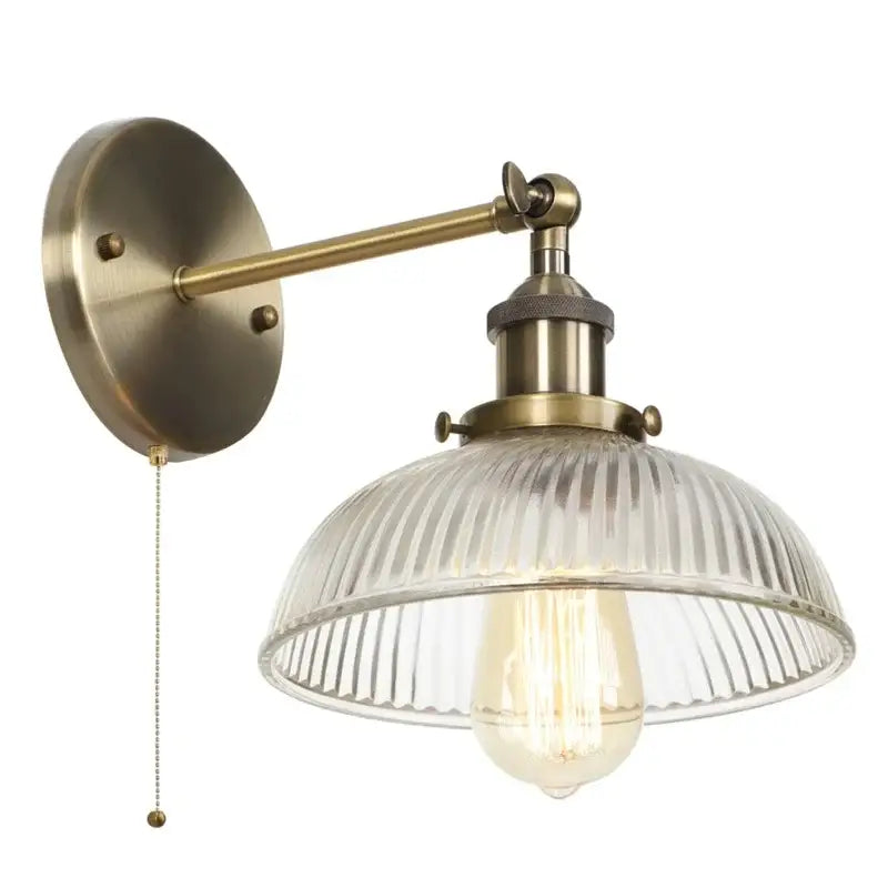Antique brass wall sconce with ribbed glass shade and exposed filament bulb featuring a pull chain switch