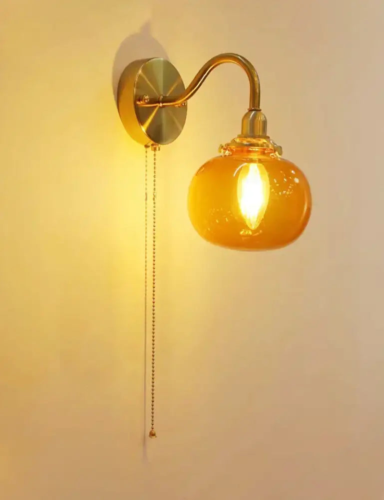 Vintage brass wall sconce lamp with warm amber ribbed glass globe and pull chain switch for bedroom lighting
