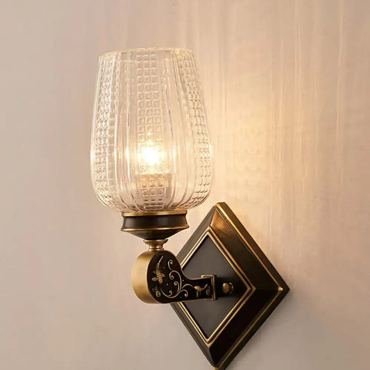 Vintage brass sconce featuring an ornate metal base with decorative inlaid patterns and clear textured glass shade
