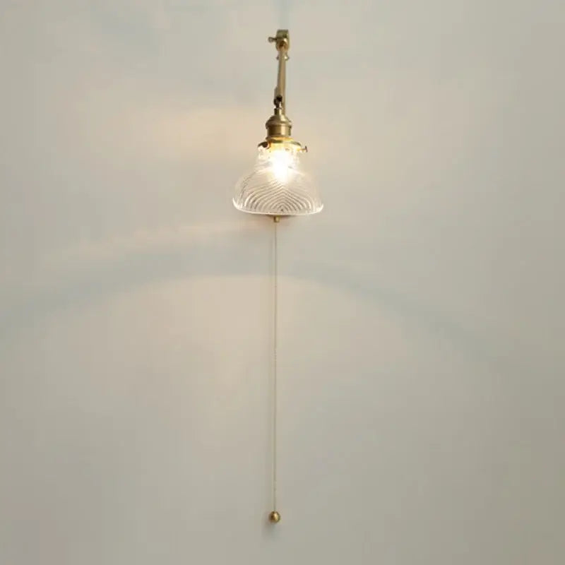 Vintage brass swing arm wall light fixture with clear textured glass shade and elegant pull chain for bedroom use