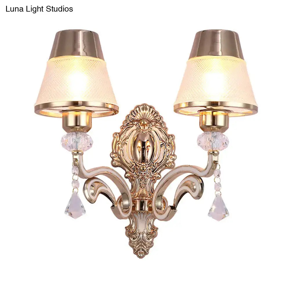 Vintage brass wall lamp with gold-toned ornate design, two crystal arms, cream cone lampshades, and clear glass shade for bedroom sconce