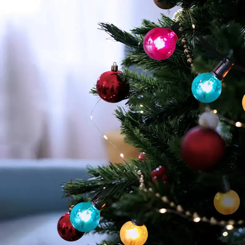 A festive christmas tree decorated with shiny red and pink ornaments illuminated by decorbites g40 edison glass string lights