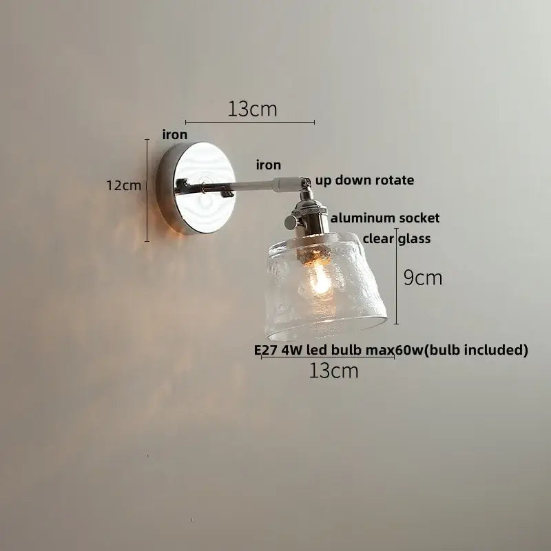 A vintage brushed nickel led wall light with a polished iron base and clear textured glass shade for bedrooms